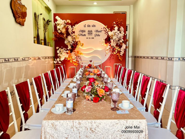 Chi Phí Trang Trí Gia Tiên Nha Trang Gồm Những Khoản Nào Bàn dài khăn trắng, ghế bọc đỏ đặt trước phông trắng đỏ trong phòng gia tiên